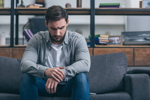 Depressiver Mann sitzt und trauert auf Couch im Wohnzimmer — Stockfoto