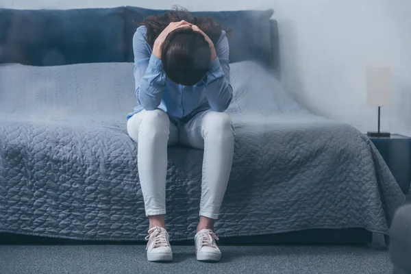 Selective focus of depressed woman sitting on bed and holding head in hands with copy space — Stock Photo