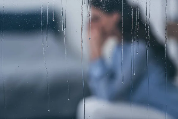 Foco seletivo de gotas de chuva em janelas com mulher triste sentada no fundo — Fotografia de Stock