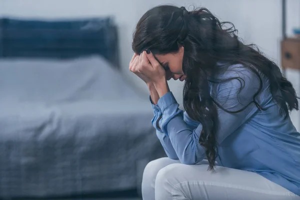 Selektiver Fokus der sitzenden Frau, die das Gesicht mit den Händen bedeckt, während sie zu Hause mit Kopierraum weint — Stockfoto