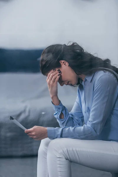 Enfoque selectivo de la mujer afligida sentada, sosteniendo la fotografía y llorando en casa - foto de stock