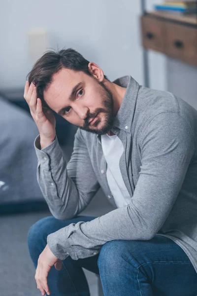 Enfoque selectivo de hombre molesto guapo sentado, tocando la cara y el duelo en casa - foto de stock