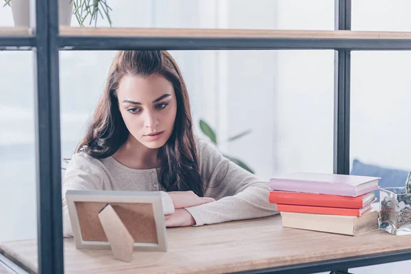 Beautiful upset woman looking at picture frame at home — Stock Photo