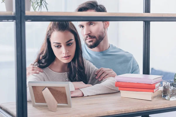 Selective focus of upset couple looking at picture frame at home — Stock Photo