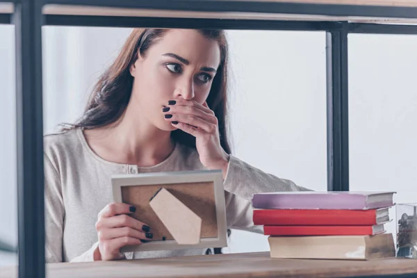 Grieving woman covering mouth with hand while holding picture frame at home — Stock Photo