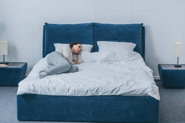 Sad lonely woman in pajamas lying in bed at home — Stock Photo