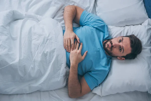 Draufsicht eines traurigen einsamen Mannes, der in die Kamera schaut und zu Hause im Bett liegt — Stockfoto