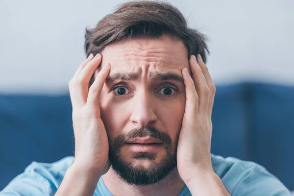 Selective focus of frightened man with hands on head looking at camera at home — Stock Photo