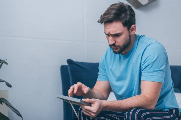 Selective focus of grieving man sitting on bed and holding photo frame at home — Stock Photo