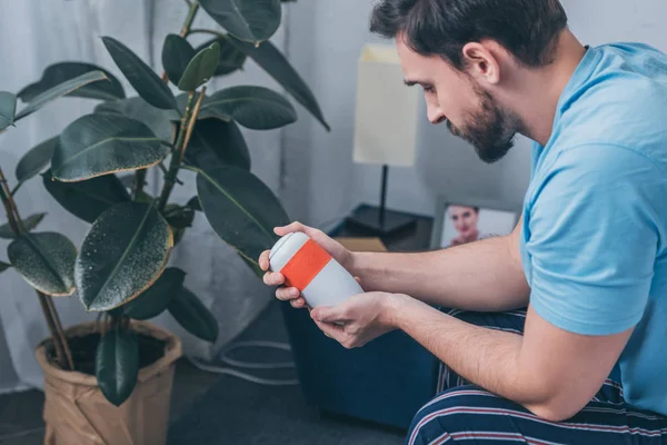 Upset man sitting and looking at funeral urn at home — Stock Photo