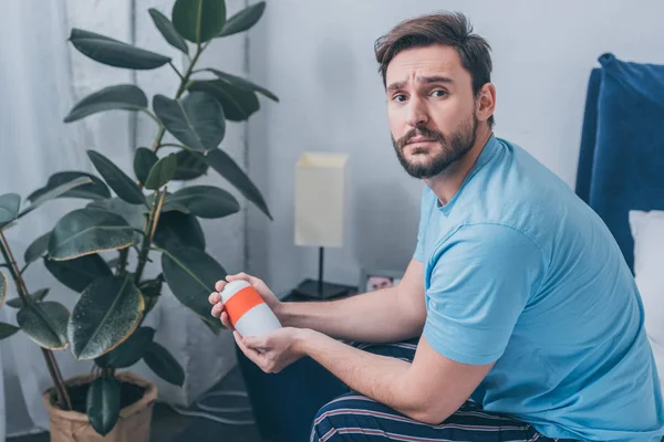 Upset man holding funeral urn and looking at camera at home — Stock Photo