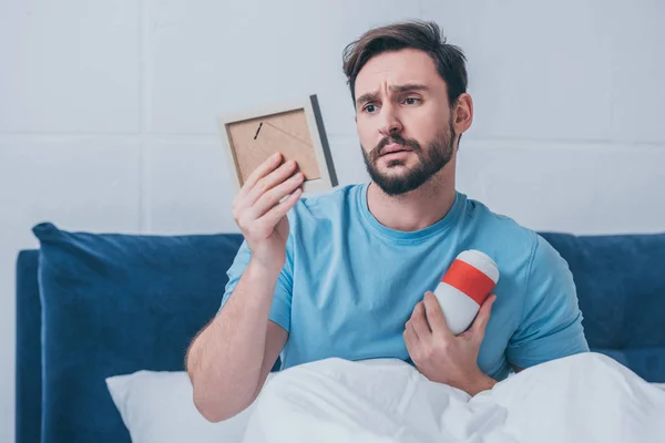 Sad man lying in bed and holding photo frame with funeral urn — Stock Photo