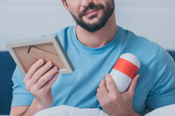 Cropped view of man holding photo frame and funeral urn at home — Stock Photo