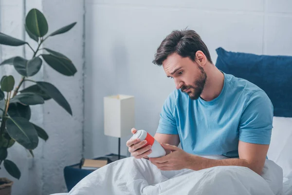 Depressed man looking at funeral urn in bed — Stock Photo