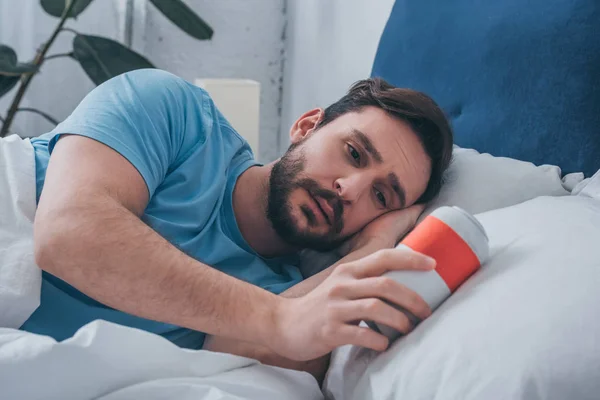 Trauernder Mann liegt im Bett und hält Urne in der Hand — Stockfoto