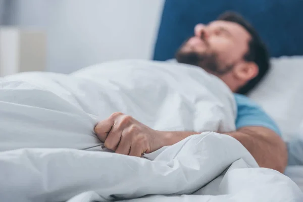 Mann liegt im Bett und hält Decke — Stockfoto