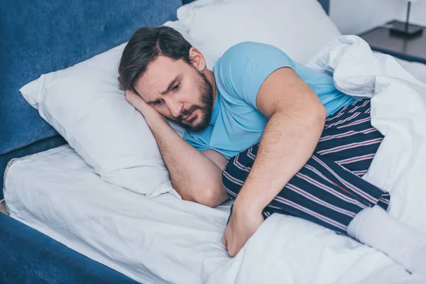 Грустный человек в пижаме скорбит, лежа в постели в одиночестве — стоковое фото