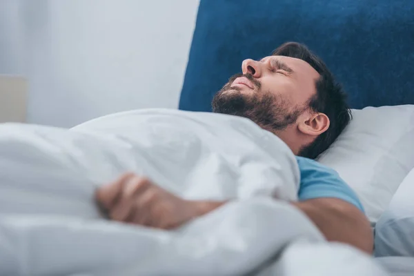 Selective focus of grieving man lying in bed and holding blanket — Stock Photo