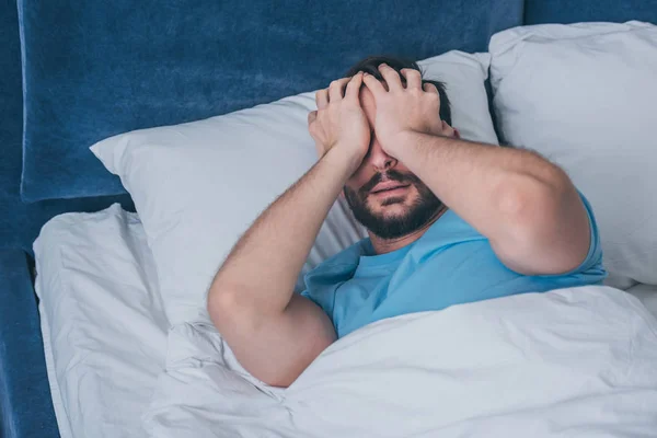 Uomo in lutto sdraiato a letto, che copre il viso con le mani e piange a casa — Foto stock