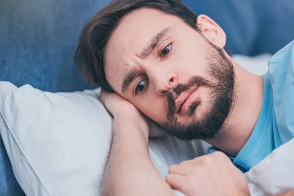 Beau homme contrarié couché dans son lit et regardant ailleurs — Photo de stock