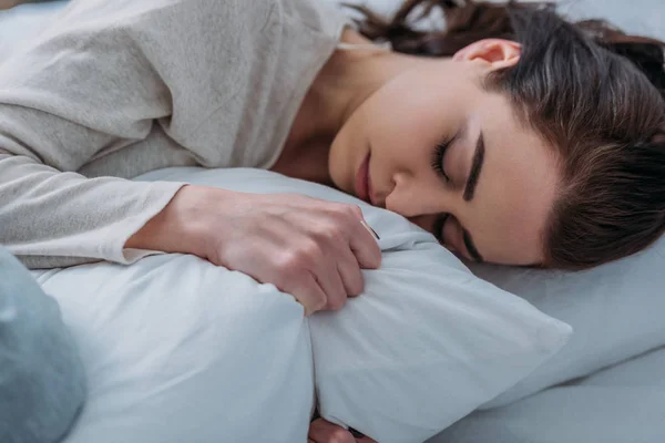 Beautiful tired woman hugging pillow and sleeping in bed at home — Stock Photo