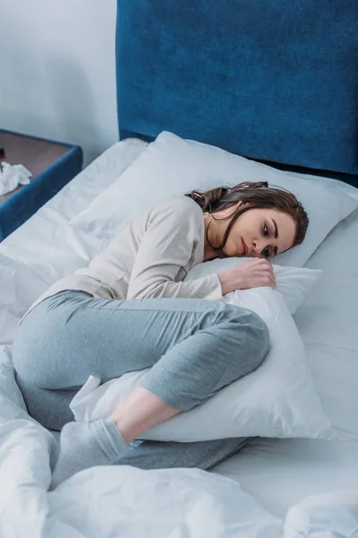 Triste mulher de pijama segurando travesseiro e deitado na cama em casa — Fotografia de Stock