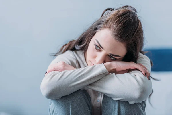 Enfoque selectivo de la hermosa mujer triste abrazando rodillas y mirando hacia otro lado - foto de stock