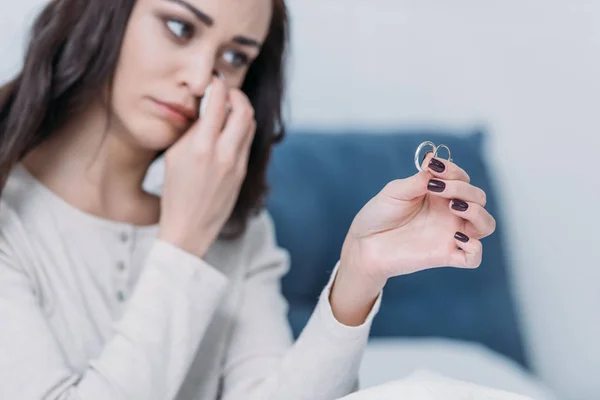 Sad woman holding wedding rings and wiping tears while crying at home — Stock Photo