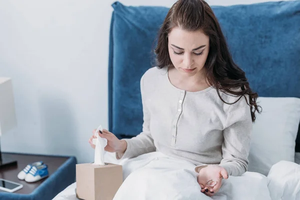 Upset woman with tissue box lying in bed and holding wedding rings — Stock Photo