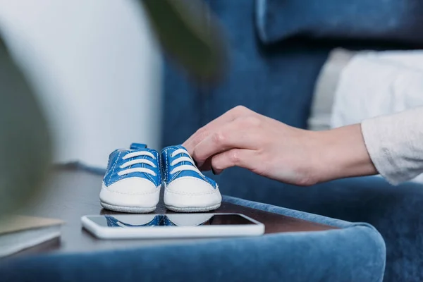 Vista recortada de la mujer sosteniendo zapatos de bebé en casa - foto de stock