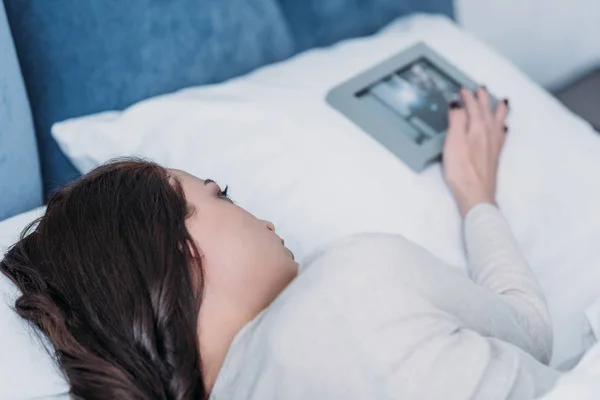 Triste mulher deitada na cama perto de quadro de imagem no travesseiro em casa — Fotografia de Stock