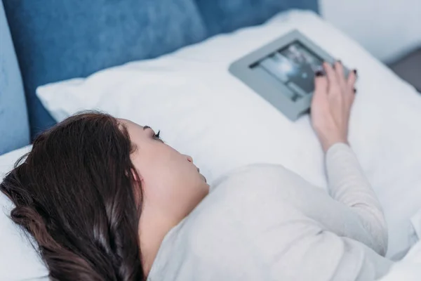 Sad woman lying in bed near picture frame on pillow at home — Stock Photo