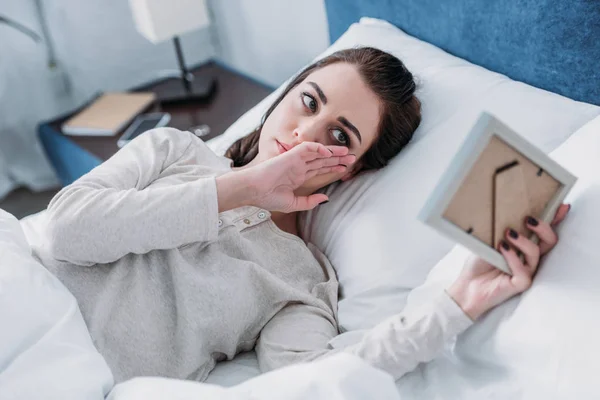 Upset woman lying in bed, looking at picture frame, crying and wiping tears at home — Stock Photo