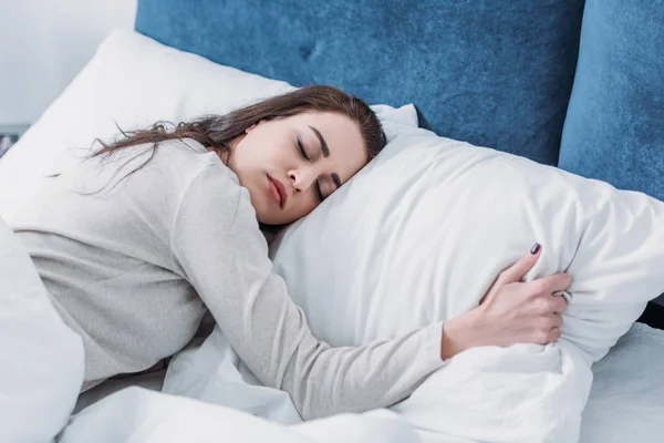 Красива втомлена жінка обіймає подушку і спить в ліжку вдома — стокове фото