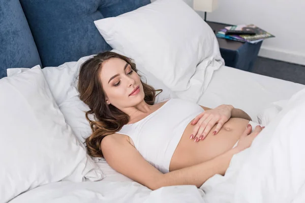 Charming pregnant woman lying in bed and touching tummy — Stock Photo
