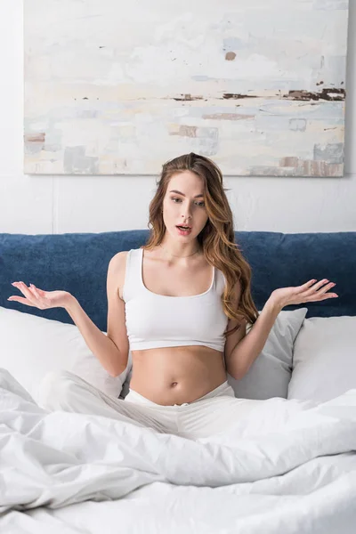 Confused pregnant woman gesturing while sitting in bed — Stock Photo
