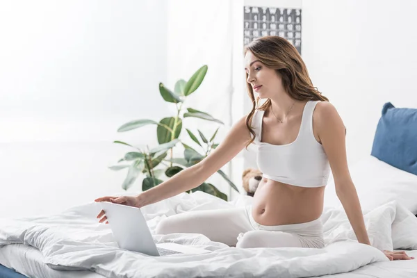 Pregnant woman sitting on bed with laptop — Stock Photo