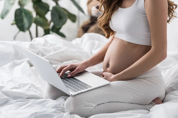 Частковий вигляд вагітної жінки, що використовує ноутбук у ліжку — стокове фото