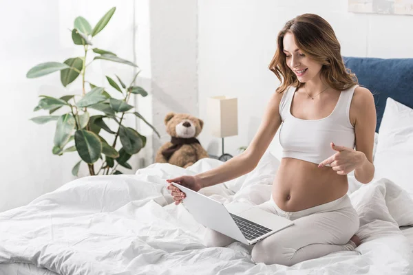 Захоплена вагітна жінка використовує ноутбук у ліжку — стокове фото
