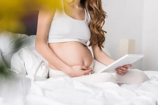 Teilbild einer langhaarigen Schwangeren mit digitalem Tablet im Bett — Stockfoto