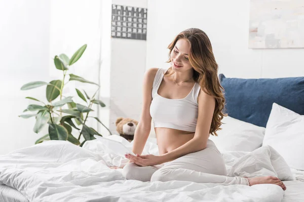 Mulher grávida sorrindo usando comprimido digital na cama — Fotografia de Stock