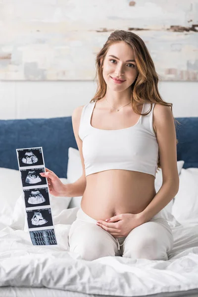 Sourire jeune femme enceinte montrant des échographies — Photo de stock