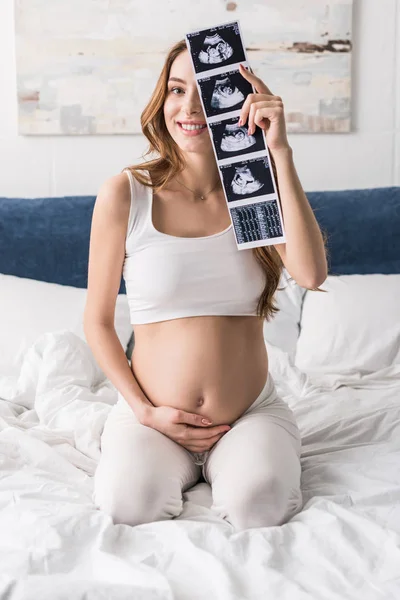 Excited pregnant woman sitting on bed with ultrasound scans — Stock Photo