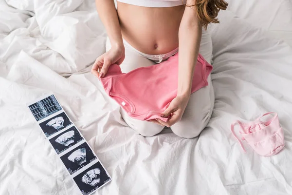 Частковий вигляд вагітної жінки, що тримає рожевий дитячий одяг — стокове фото