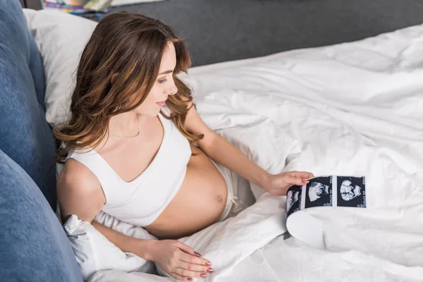 Pregnant young woman lying in bed and looking at ultrasound scans — Stock Photo