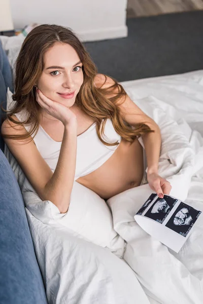 Feliz mulher grávida deitada na cama com exames de ultra-som — Fotografia de Stock