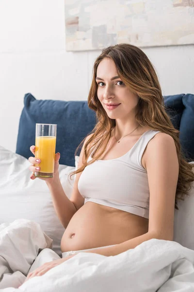 Mujer joven embarazada bebiendo jugo en la cama - foto de stock