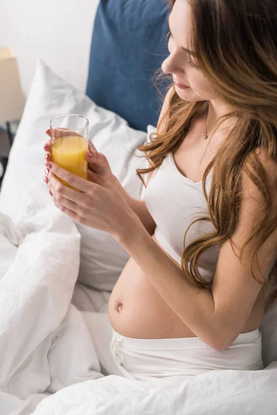 Mujer joven embarazada bebiendo jugo en la cama - foto de stock