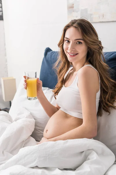 Happy pregnant young woman drinking juice in bed — Stock Photo