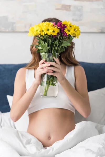 Donna incinta in possesso di vaso con fiori mentre seduto a letto — Foto stock